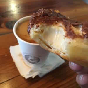 bite taken out of custard-filled donut with coffee in background