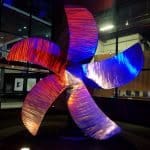 large brushed steel fan blade colored by red and blue lights at night