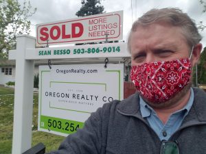 man standing in front of real estate sign wearing a protective mask